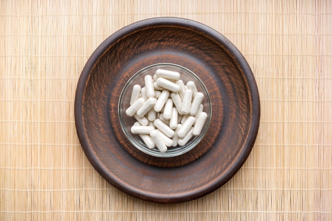 Wooden Bowl With Ashwagandha Capsules on Bamboo Mat to Represent Answer to Question What are Adaptogens | Vitacost.com/blog
