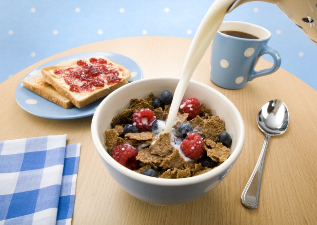 Enjoying the Benefits of Breakfast with Milk Pouring from Pitcher into Bowl of Berry-Studded Cereal | Vitacost.com/blog