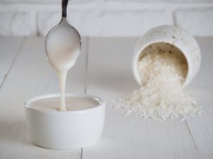 How to Make Coconut Butter Illustrated by Coconut Shreds in Jar and Coconut Butter Dripping From Spoon into White Bowl | Vitacost.com/blog