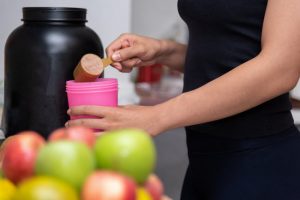 Torso View of Woman Trying to Save Money on Sports Nutrition Products Scooping Protein Powder into Shaker Cup | Vitacost.com/blog