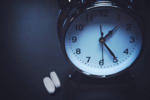 Alarm Clock and Supplements on Table in Dimly Lit Setting to Represent Melatonin Benefits for Sleep | Vitacost.com/blog