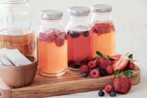 Glass Bottles of Kombucha and Fruit on Wooden Cutting Board to Demonstrate Gut Health Foods | Vitacost.com/blog