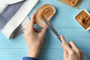Overhead View of Hands Spreading Nut Butter on Bread to Demonstrate Healthy Mix of Carbs and Fat | Vitacost.com/blog