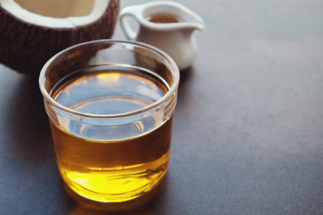 MCT Oil Benefits, Uses and How it Compares to Coconut Oil MCT Oil in Small Glass Cup on Black Table with Coconut and Small Pitcher of Coconut Oil | Vitacost.com/blog