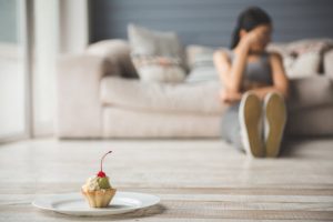 Woman Quitting Sugar Trying to Resist Eating a Tempting-Looking Cupcake on a Plate | Vitacost.com/blog