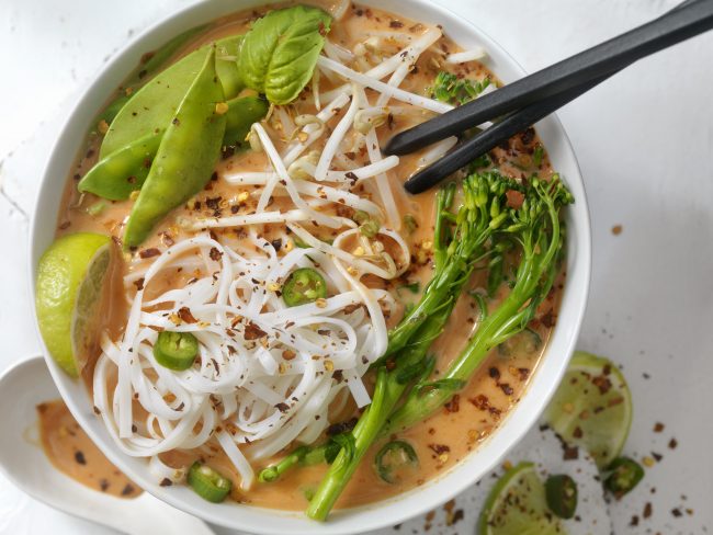 Vegan Red Curry Noodle Soup (Gluten-Free) Top View of Red Curry Soup With Noodles and Veggies on White Table | Vitacost Blog