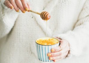 Woman in White Sweater Practicing Healthy Living Pouring Raw Honey Into Mug of Tea | Vitacost.com/blog