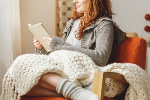Red-Haired Woman Enjoying Healing Words of Poetry Curled Up With Blanket on Chair | Vitacost.com/blog
