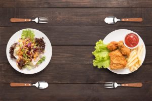 Overhead View of Two Plates with Fried Foods and Healthy Salad Alternative on Dark Wood Table | Vitacost.com/blog