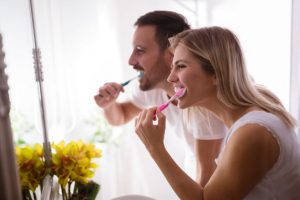 Pajama-Clad Young Couple Not Thinking About Is Fluoride Bad for You Happily Brushing Teeth in Mirror | Vitacost.com/blog