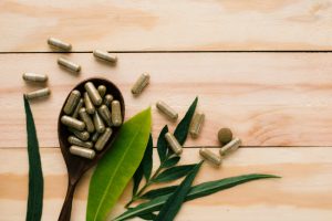 Question of What are Herbal Supplements Answered by Image of Green Capsules on Spoon With Leaves on Wooden Table | Vitacost.com/blog