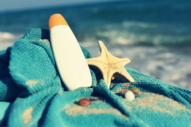 Sunscreen Facts Represented by Bottle of Sunscreen, Starfish & Shells on Teal Towel at Beach | Vitacost.com/blog