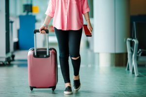 Traveling Woman Following Jet Lag Remedies Advice Pulling Pink Suitcase on Wheels Through Airport | Vitacost.com/blog