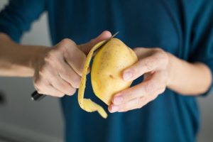 Close-up View of Man Aware of Potato Nutrition Facts Peeling Large Yellow Potato | Vitacost.com/blog