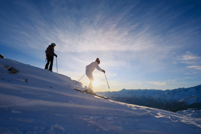 The Benefits of Skiing: 7 Life Lessons Learned on the Slopes Two Women Enjoying the Benefits of Skiing While Gliding Down Mountain at Sunset | Vitacost.com/blog