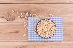 Health Benefits of Peanuts Represented by Overhead View of Bowl of Nuts on Blue-and-White Checked Napkin on Wooden Table | Vitacost.com/blog