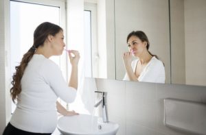 Pregnant Woman Brushing Teeth in Mirror Wondering if She Should Visit a Dentist During Pregnancy | Vitacost.com/blog