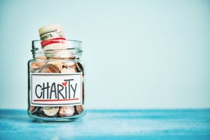 Example of Ways to Give: Coins and Cash Donations Stuffed in Charity Jar on Blue Table | Vitacost.com/blog