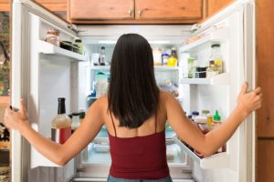 Woman Following Intermittent Fasting Tips Standing in Front of Fridge Considering Best Foods to Break a Fast | Vitacost.com/blog