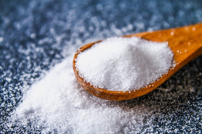 Wooden Spoon Overflowing with Salt on Blue Table to Represent Concept of Monitoring Sodium Levels | Vitacost.com/blog