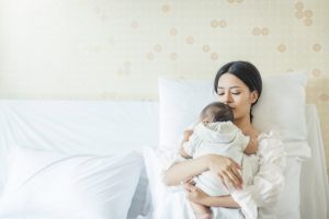 Post Pregnancy New Mother Tenderly Cuddling Newborn Baby While Propped up on Pillows in Bed | Vitacost.com/blog