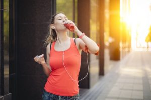 Woman Wearing Headphones Preventing Electrolyte Imbalance Drinking Sports Drink On City Street | Vitacost.com/blog