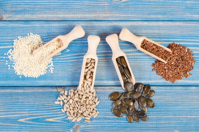 Seed Cycling for Hormone Balance Represented by Wooden Scoops Filled With Various Types of Seeds on Blue Wood Table | Vitacost.com/blog