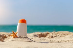 View of Reef Safe Sunscreen Bottle and Starfish on Sand at Beach with Blurred Ocean in Background | Vitacost.com/blog
