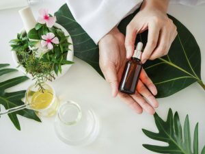 Overhead Shot of Various Botanicals, Glass Beaker, Mortar, Pestle and Hands Holding Brown Bottle to Represent Argan Oil Benefits | Vitacost.com/blog