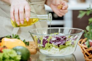 Woman Pouring Oil Over Salad in Glass Bowl as Example of One of Many MCT Oil Uses | Vitacost.com/blog