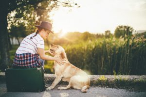 Woman Sitting on Suitcase Petting Dog During Summer Travel to Countryside | Vitacost.com/blog
