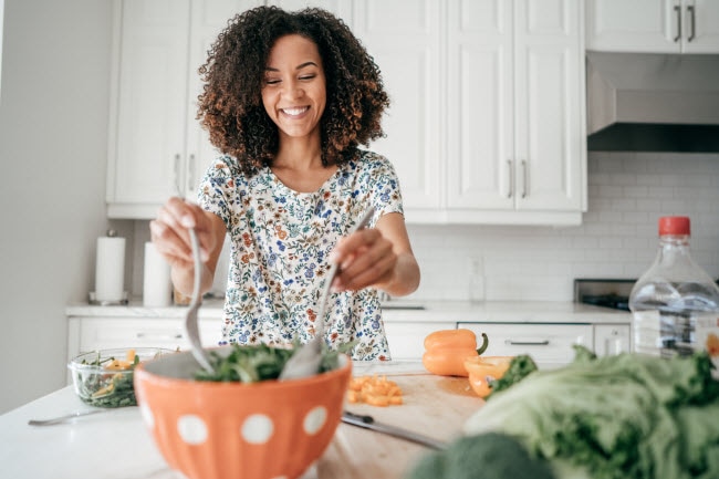 Smiling Woman Following AIP Diet, Autoimmune Protocol Diet, in Kitchen Preparing Salad in Orange Bowl | Vitacost.com/blog