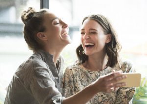 Two Women Enjoying the Benefits of Laughter and Each Other's Company While Looking at Pictures on Phone | Vitacost.com/blog
