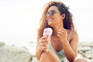 Smiling Woman Eating Ice Cream Cone at Beach Not Yet Thinking About How to Get Back on Track With Diet After Vacation | Vitacost.com/blog