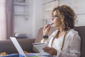 Woman Learning How to Focus Better Working on Laptop While Sitting on Couch Biting Pen | Vitacost.com//blog