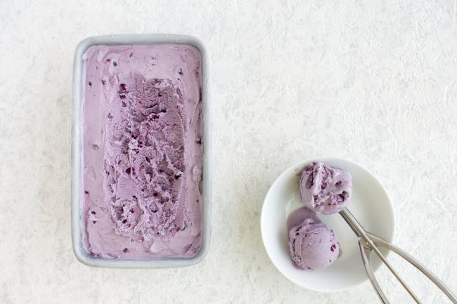 How to Make Dairy Free Ice Cream Represented by Blueberry Ice Cream Being Scooped From Tin on White Countertop | Vitacost.com/blog