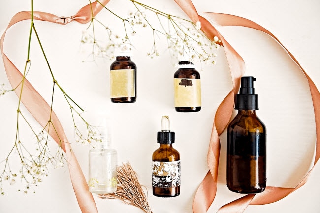 Variety of Amber Face Serum Bottles on White Surface With Dried Flowers and Ribbon | Vitacost.com/blog