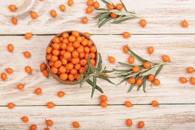 Cup Full of Tiny Orange Berries with Sprigs of Greenery on Wooden Table to Represent Sea Buckthorn Oil Benefits | Vitacost.com/blog