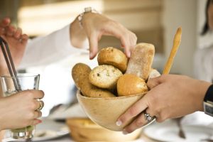 Woman With Carb Addiction Grabbing Roll From Basket of Bread Being Passed to Her at Restaurant | Vitacost.com/blog