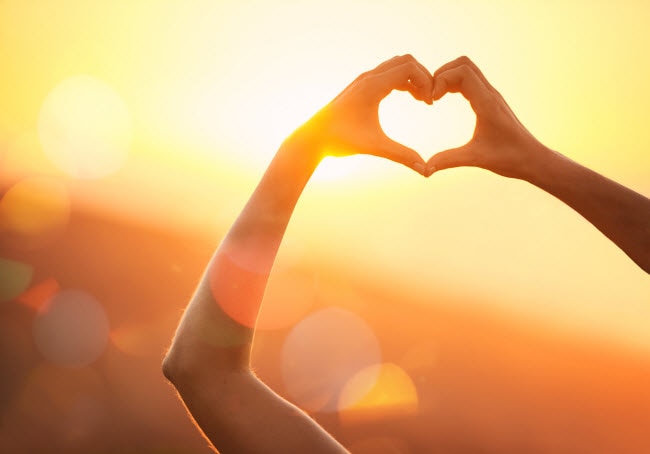 Woman With Hands Forming Heart Shape Standing Outside Enjoying the Benefits of Sunlight | Vitacost.com/blog