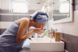 Woman Wrapped in Blue Towels Learning How to Treat Acne Using the Best Products for Adult Acne While Washing Face | Vitacost.com/blog
