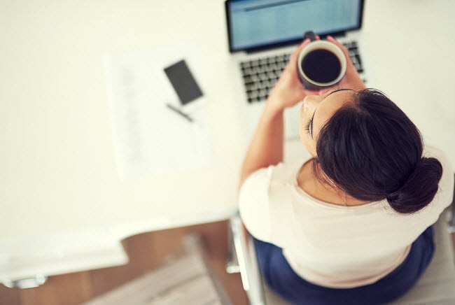 Overhead View of Woman Concerned About Workplace Health Sitting at Office Desk With Laptop & Coffee | Vitacost.com/blog