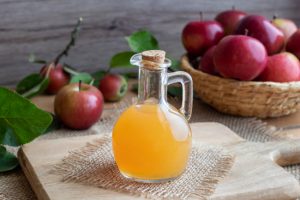 Apple Cider Vinegar Uses Exemplified by Glass Jar of ACV on Fiber Mat Surrounded by Red Apples on Wooden Table | Vitacost.com/blog