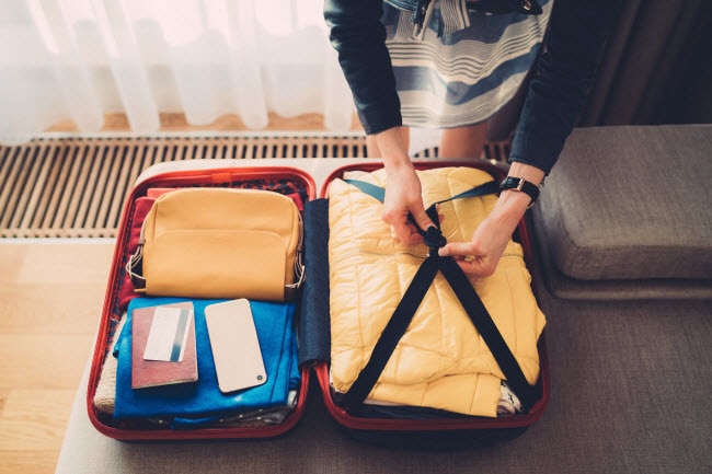Woman Following Travel Tips on Ways to Reduce Waste Packing Suitcase on Hotel Bed | Vitacost.com/blog