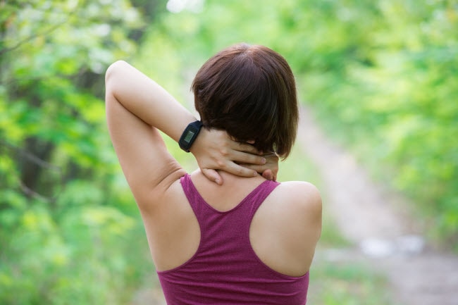 Back View of Short-Haired Woman in Wooded Area Stretching and in Need of Neck Pain Relief | Vitacost.com/blog