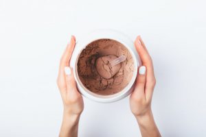 Woman's Hands Holding Chocolate Protein Powder Container to Represent Question of How Much Protein is Too Much | Vitacost Blog