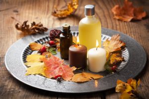 How to Use Essential Oils During the Fall Season Represented by Lit Candles, Bottles and Autuman Leaves on Brushed Silver Platter on Wooden Table | Vitacost.com/blog