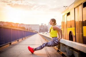 Athletic Woman in Workout Clothes Doing Simple Exercises on Her Daily Commute Beside a Bus on a City Street | Vitacost.com/blog