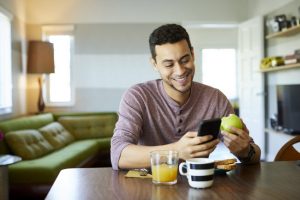 Man Eating Healthy Breakfast at Table While Reading Male Fertility Tips on Mobile Phone | Vitacost.com/blog