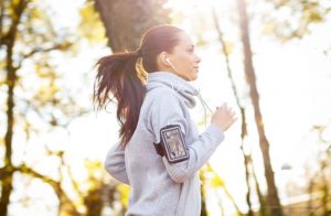 Woman with Ponytail and Headphones Jogging in Afternoon Sunlight in Woods as Part of Weekend Warrior Workout | Vitacost.com/blog